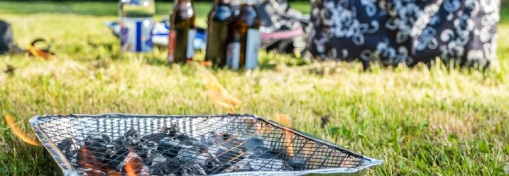 Einweggrill mit glühender Kohle auf einer Wiese im Freien.